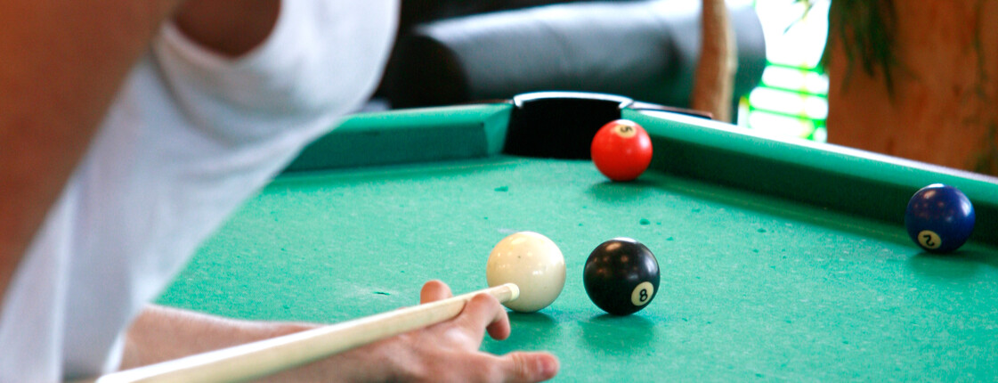 Eine Jugendlicher mit weißen T-Shirt und Cap beim Billard spielen.