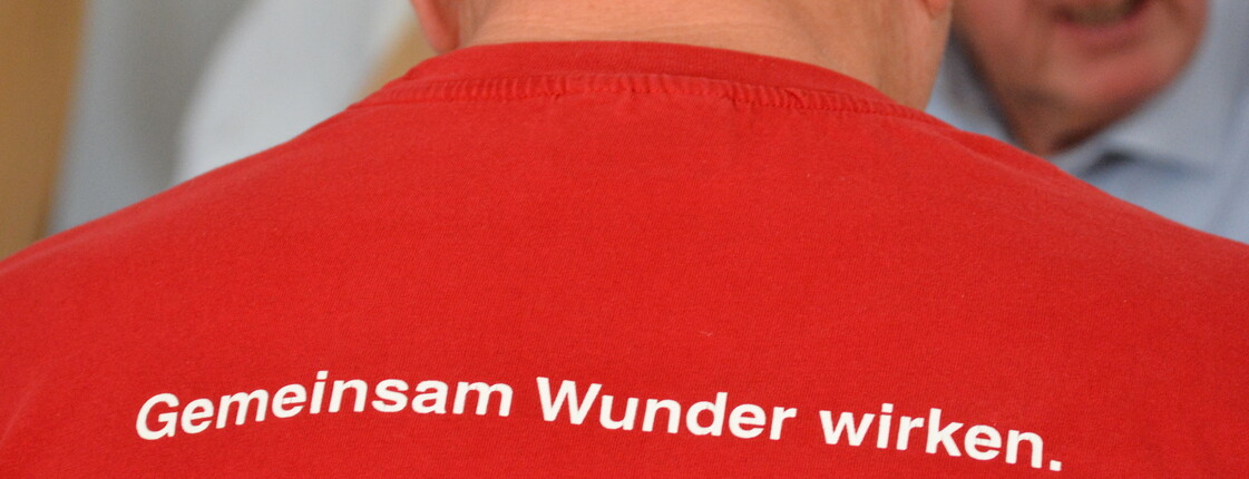 Ein Mann trägt ein T-Shirt mit der Aufschrift "Gemeinsam Wunder wirken"