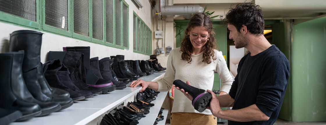 Ein Mann und eine Frau stehen in einem Second Hand Shop vor Regalen mit schwarzen Schuhen und suchen gemeinsam Schuhe aus.